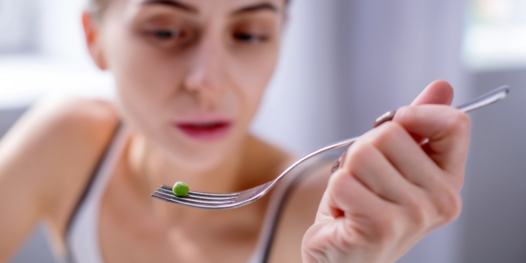 En person holder en gaffel med en enkelt grøn ært.